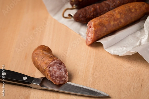 Fototapeta Ringwurst Salami und Bierbeißer Wurst in Wachspapier mit Messer auf Vesper Holzbrett