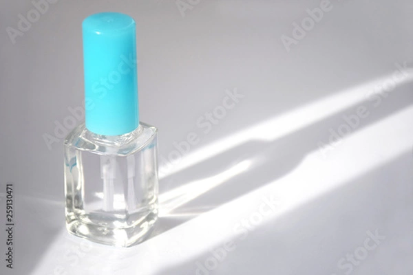 Fototapeta Closed bottle of clear nail polish for manicure. Clear transparent nail polish bottle with blue cap. Manicure concept. Sunbeam illuminates a bottle of nail polish with copy space, moke up.