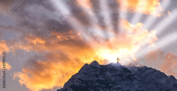 Fototapeta Silhouette of a cross on the top of a mountain with sun rays and dramatic clouds in the background. Symbol of God, religion, resurrection,miracle and faith. 