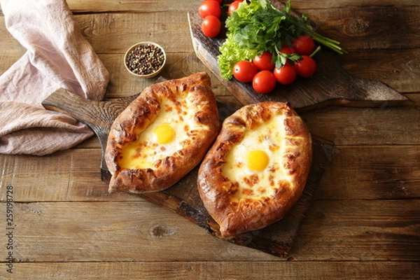 Fototapeta Two Khachapuri Adjara traditional Georgian dishes. Baked bread stuffed with cheese and eggs. With copy space for text. Flat lay. Top view. 