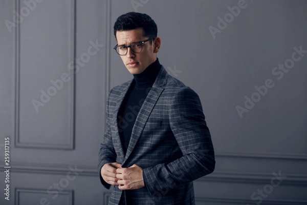 Fototapeta Handsome,fit man in gray suit with black turtleneck,black stylish eyeglasses looks confident at the camera.