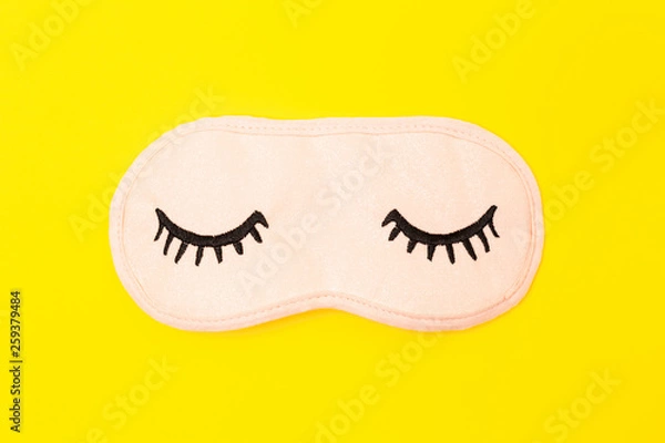 Fototapeta Pastel pink sleep mask with closed eyes embroidered on it with eyelashes on bright yellow neon paper background. Top view, flat lay. Concept of vivid dreams. Accessories for girls and young women.