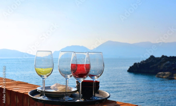 Fototapeta four glasses of white and red wine in front of the beach and romantic seaside, aperitif moment in Tellaro, Liguria Italy