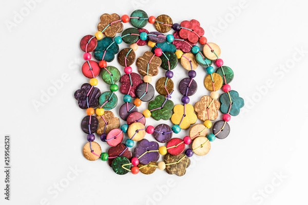 Fototapeta Multi colored beads hand made from coconut shell, flowers and rounded pieces, traditional African decoration isolated on white background, top view, flat lay