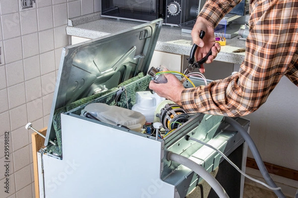 Fototapeta People in technician jobs. Appliance repair technician or handyman works on broken dishwasher in a kittchen. Laborer is changing the heating element.