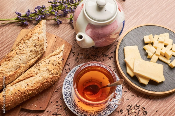 Fototapeta Cup of tea with cheese and bread next to a teapot