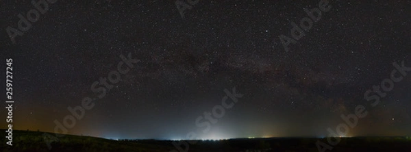 Obraz Stars of the Milky Way in the night sky. Light pollution from street lamps above the horizon.