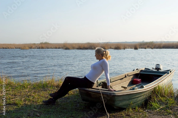 Obraz The Woman Sits On A Boat On The Lake Shore