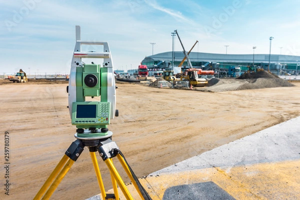 Fototapeta Surveyor engineer with equipment (theodolite or total positioning station) on the construction site of the road or building with construction machinery background