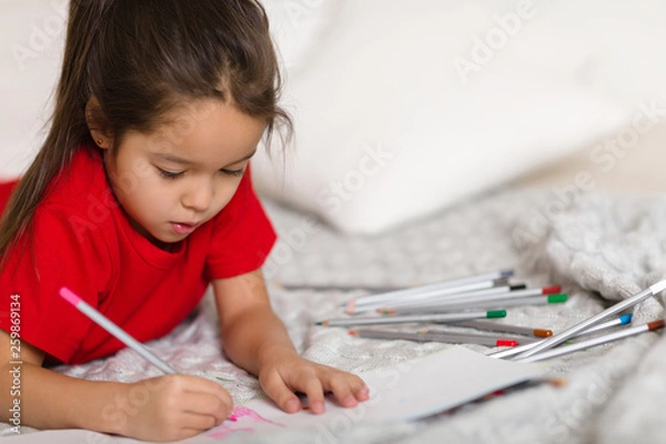 Fototapeta cute little child girl in red pajamas draws with pencils at home