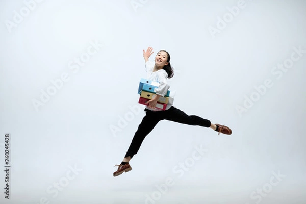 Fototapeta Happy to try something new. Woman working at office, jumping and dancing in casual clothes or suit isolated on white studio background. Business, start-up, working open-space concept.