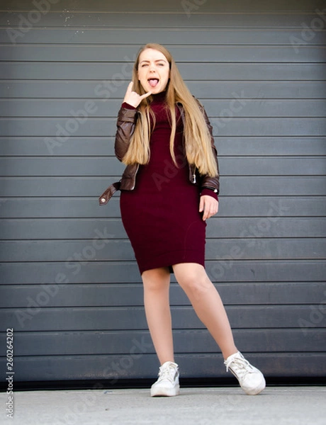 Obraz Portrait of a beautiful girl in a dark red dress knee-deep and in a dark leather jacket in the street in the afternoon