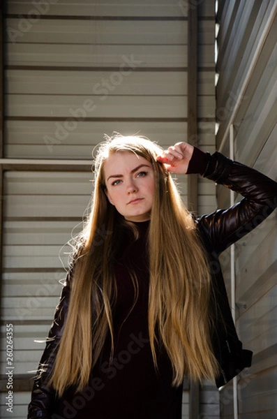 Obraz Portrait of a beautiful girl in a dark red dress knee-deep and in a dark leather jacket in the street in the afternoon