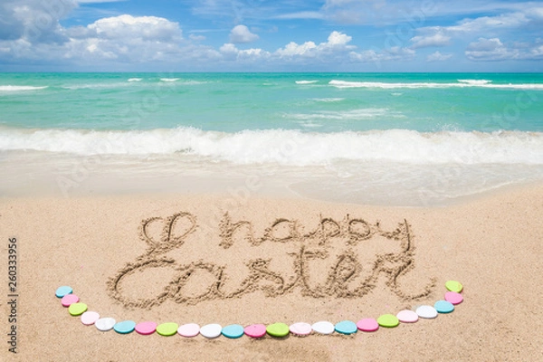 Fototapeta Happy easter lettering background with eggs on the sandy beach
