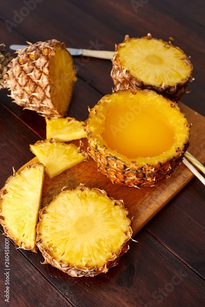Fototapeta Fresh fruit juice with exotic pineapple on a wooden brown table. A composition made of ananas. Top wiev. 
