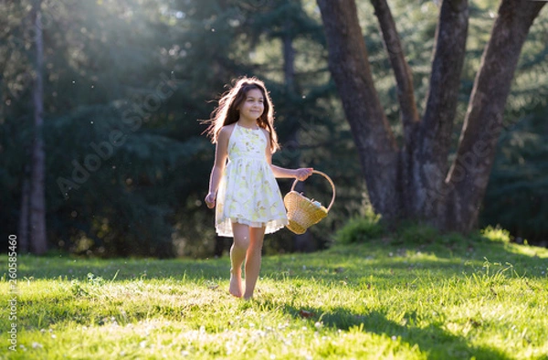 Fototapeta Little girl is walking holding woven basket with Easter pastel eggs