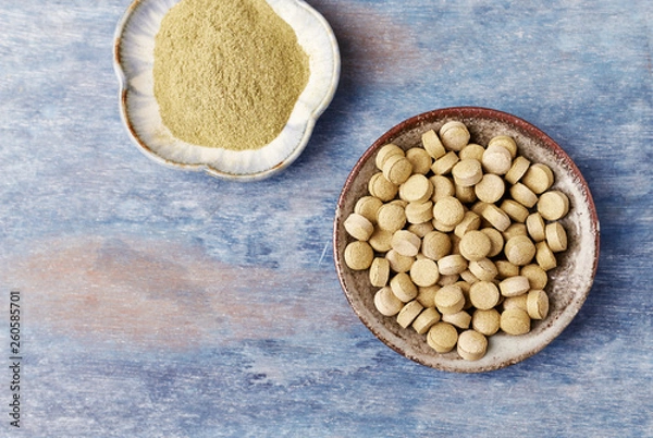 Fototapeta Bio Green BARLEY GRASS tablets and powder. Concept for a healthy dietary supplementation. Rustic wooden background. Top view. Copy space. 