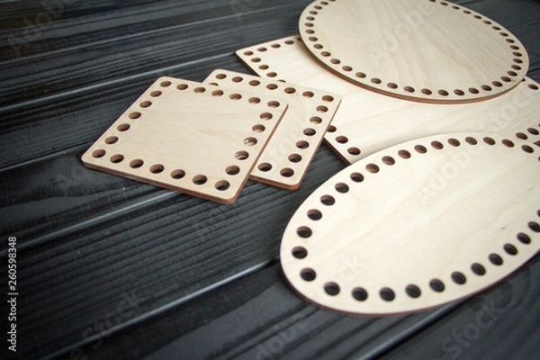 Fototapeta Light wooden parts with holes for making handmade knitted bags on a black surface. Selective soft focus.
