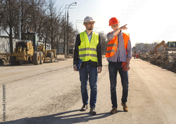 Fototapeta two men are builders workers are engineers at a construction site are looking at the drawings in helmets