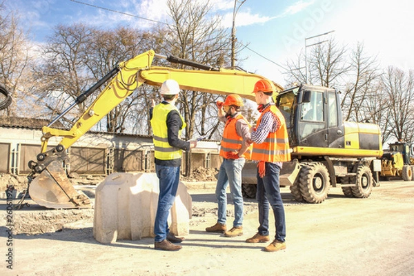 Fototapeta male workers engineers in helmets talking near the bulldozer and excavator