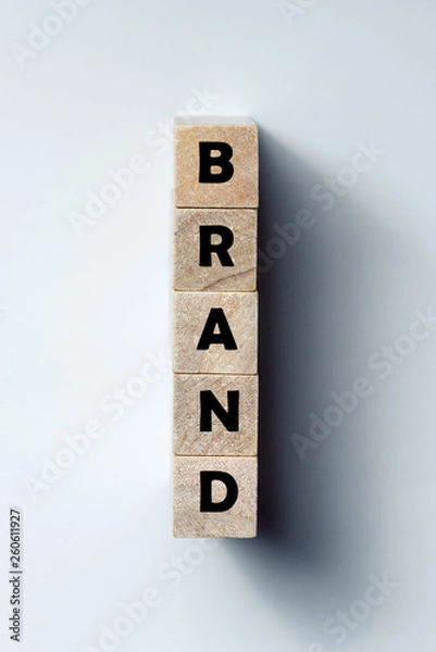 Fototapeta a line of wooden cubes with the inscription "brand", on an uneven white background. Vertical frame