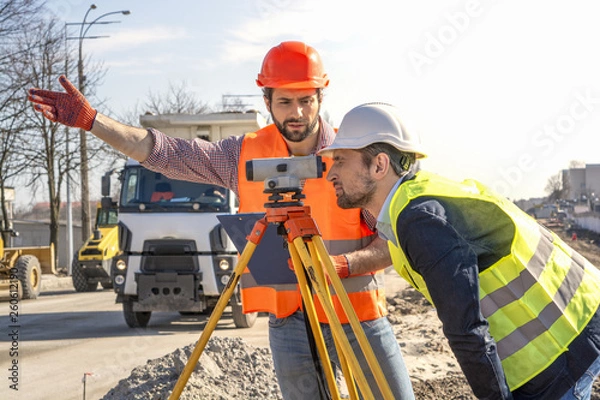 Fototapeta two male surveyor engineer with a device working on a construction site in a helmet