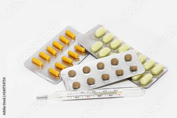 Fototapeta multi-colored yellow orange brown pills and a temperature thermometer on a white background