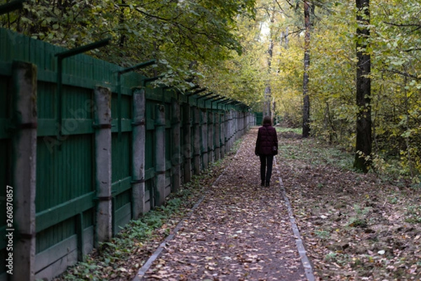 Fototapeta A track along a prison fence. Man walking down the path past the barbed wire.