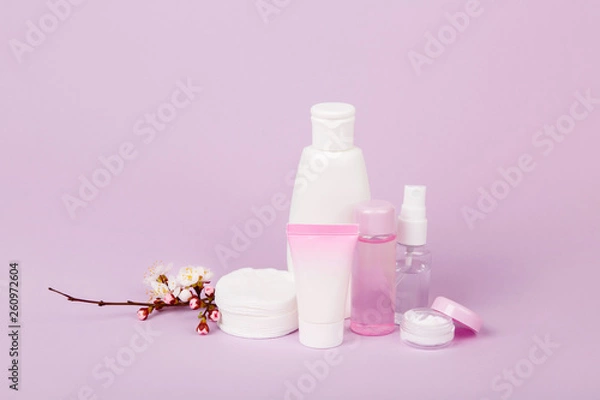 Fototapeta Face and body care products with spring bloom (tonic or lotion, serum, cream, shampoo, micellar water, cotton pads and sticks, shaver) on purple. Freshness and body care. Skin cosmetics. Border banner