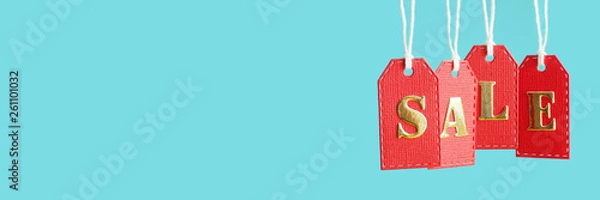 Obraz inscription sale in gold letters on red hanging labels on a blue background  in popular social media banner proportions. copy space...
