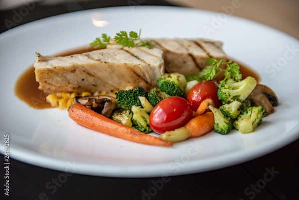 Fototapeta A grilled chicken served with broccoli, red tomato, carrot, mushroom and corn in Asian style. Served as a main course in a modern French restaurant in Bangkok, Thailand.