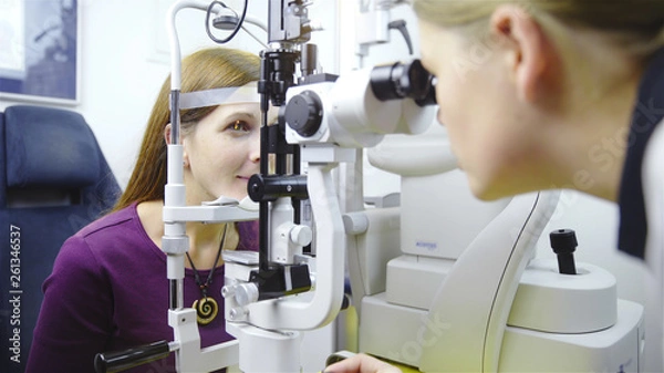 Fototapeta Female optometrist looking inside the device of patient eyeballs