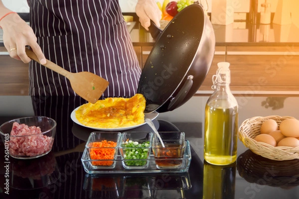 Obraz Young man turn pan and use wood spatula to flip omelette out onto the plate,making breakfast in the morning. New generation modern lifestyle concept.
