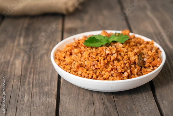 Fototapeta Buckwheat porridge with a sprig of parsley in a bowl on a dark rough wooden table. traditional Russian dish. Rustic style. Copy space.