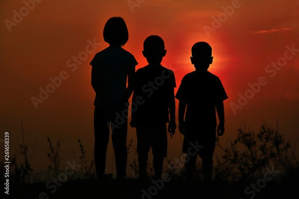 Obraz Black silhouette of three children standing together. There is a sky at sunset.