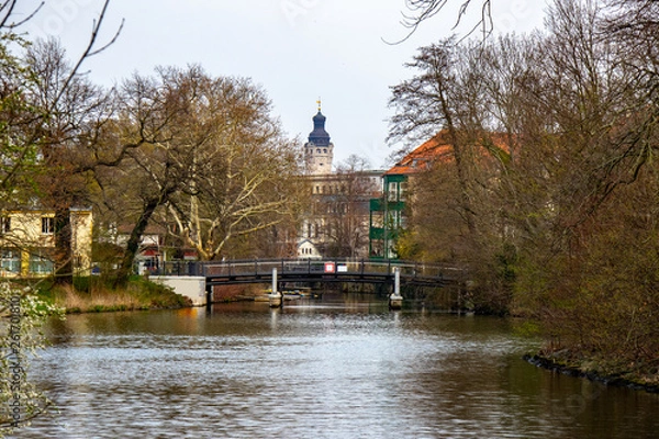 Fototapeta View of a bridge over the river "Weisse Elster" in Leipzig with trees and the New Town Hall in the background