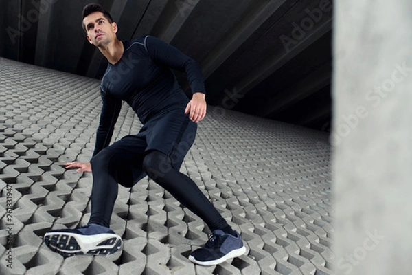 Obraz Sports man climbing at concrete grey wall, and doing his training in urban area scenery. Concept of achieve goals.