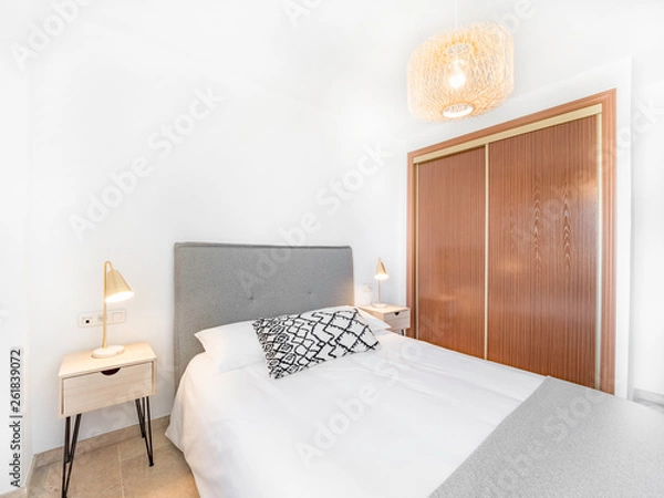 Fototapeta Comfortable hotel bedroom with felt headboard with natural fabric cushion, rattan lamp, wood nightstand and a big wooed wardrove.Holiday destination apartment with scandinavian style.