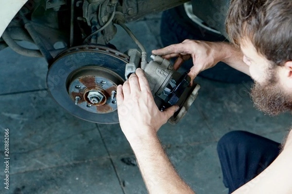 Fototapeta A car mechanic installing new brake pads on a car wheel hub