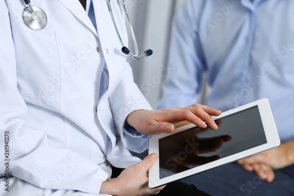 Fototapeta Female doctor using touchpad or tablet computer while consulting man patient in hospital. Medicine and healthcare concept