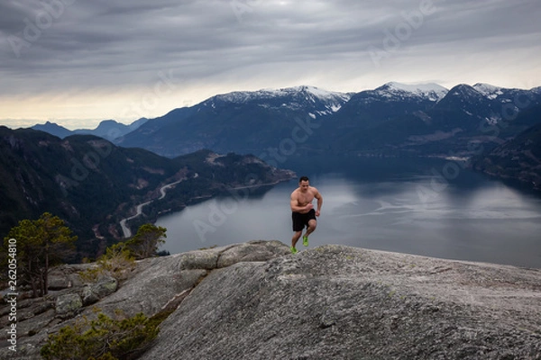 Fototapeta Fit and Muscular Young Man is Running up the Mountain during a cloudy day. Taken on Chief Mountain in Squamish, North of Vancouver, BC, Canada.