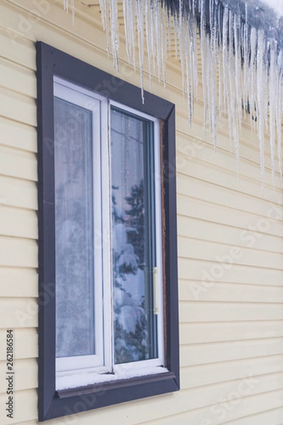 Fototapeta Icicles hang from the roof of a private house in winter