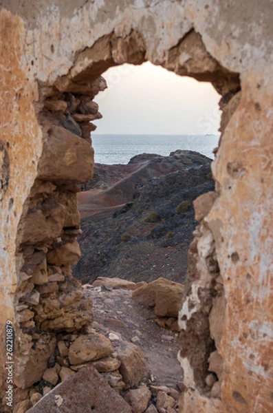 Fototapeta Wall with gate of a building demolished on a cliff facing the sea