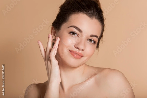 Obraz Beautiful face portrait of young woman is applying face cream on a cheek. Skin care and health concept.