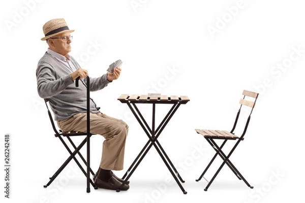 Fototapeta Senior man with a cane sitting at a table and playing cards