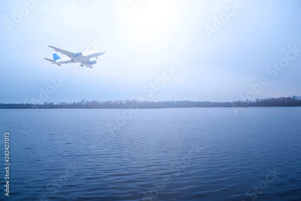 Obraz Airliner over the river in a cloudy dark sky. The sun shines brightly.