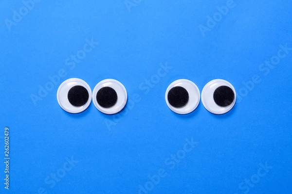 Fototapeta Googly eyes: Two pair strabismus and squint mad googly eyes next to each other on a blue background.