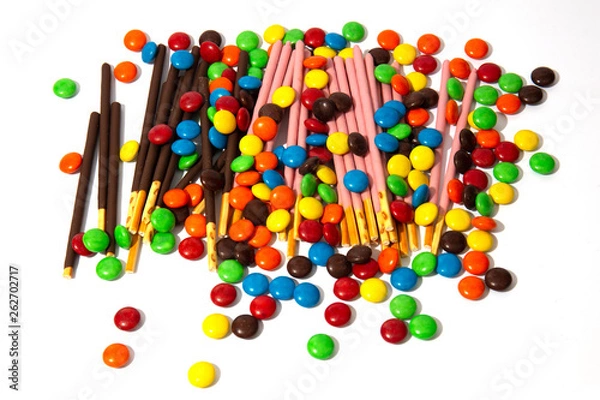 Fototapeta Colorful chocolate M&Ms and Pocky candy in and out of focus on white background