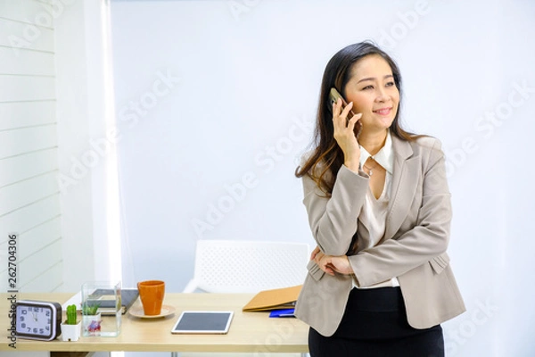 Fototapeta businesswoman talking on mobile phone while standing by window in office.