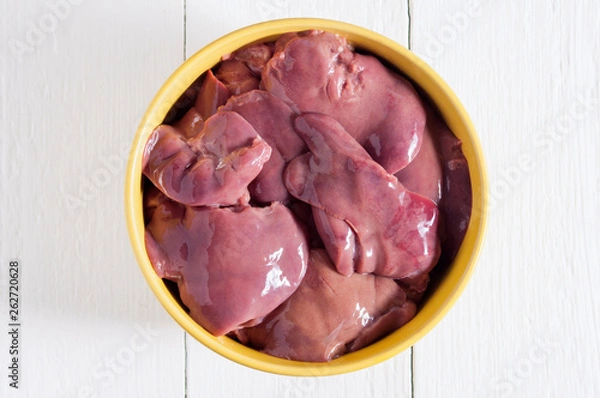 Fototapeta Raw chicken liver in a yellow bowl on a white wooden table. Top view.